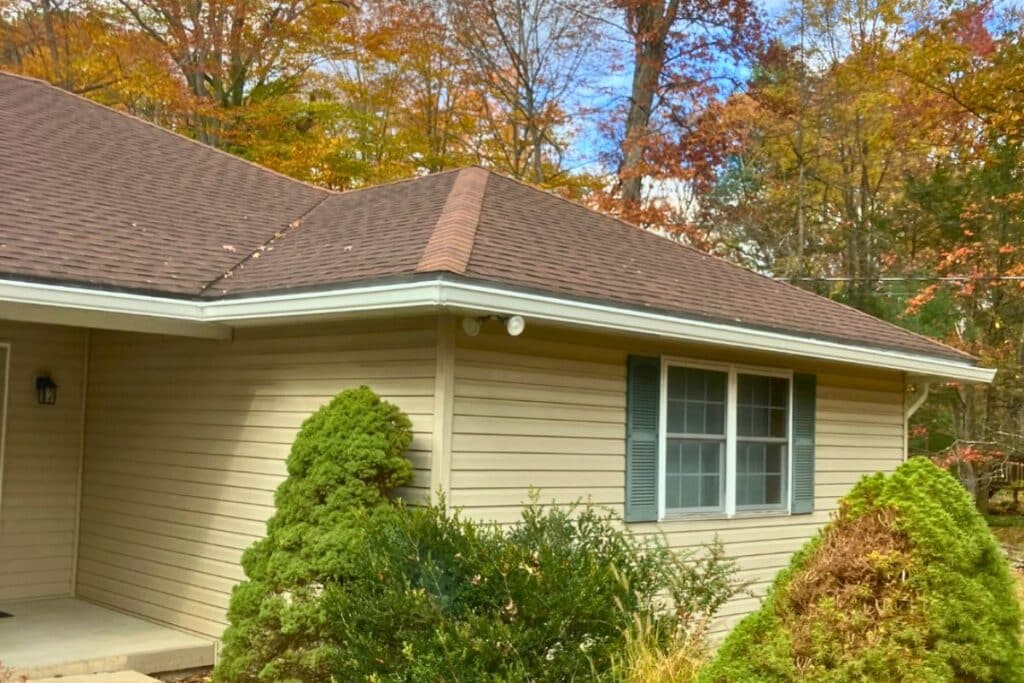 residential home with aluminum gutter system and surrounding trees in fall